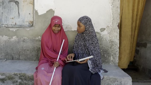 Young blind woman being assisted in learning, by her friend at her home. Zanzibar. Africa.