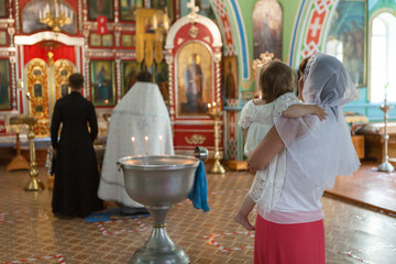 Godmother with her goddaughter on arms standing close to baptistery during baptism ceremony in Russian small church