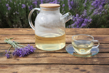 Tasty herbal tea and fresh lavender flowers on wooden table in field