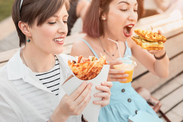 Two happy women friends relaxing in city park and eating modern street food cuisine. Healthy diet...