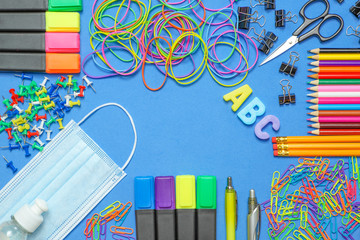 School stationery supplies with medical mask and hand sanitizer on blue background. Back to school...