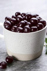 Fresh acai berries in mug on light grey table, closeup