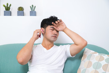 Sad unhappy handsome man sitting on the sofa and putting his hand on forehead and using ear...