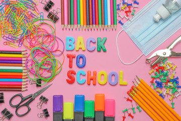 School stationery supplies with medical mask and hand sanitizer on pink background. Back to school...