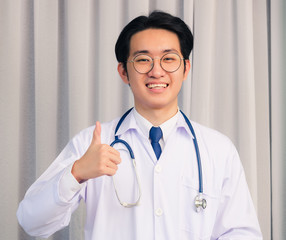 Portrait closeup of Happy Asian young doctor handsome man smiling in uniform and stethoscope neck strap show finger thumb up and see to the camera, Healthcare medicine concept