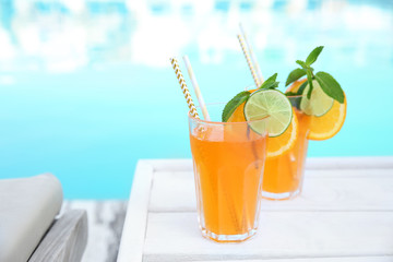 Refreshing cocktail in glasses near outdoor swimming pool on sunny day. Space for text