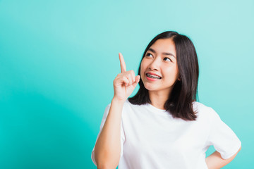 Portrait of Asian teen beautiful young woman smile have dental braces on teeth laughing point finger side away blank copy space, studio shot isolated on blue background, medicine and dentistry concept