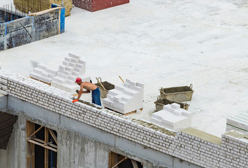 Bricklayer worker makes a wall of white silicate bricks on a construction site of a big residential...