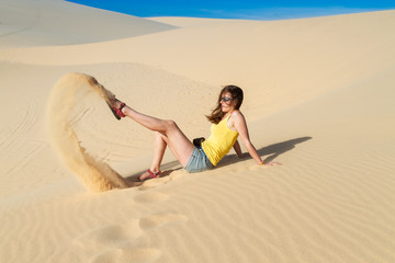 Woman sits on the sand in the desert, wearing a T-shirt and shorts. Playing with sand.