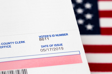 Closeup of voter registration identification card with American flag in background. Concept of...