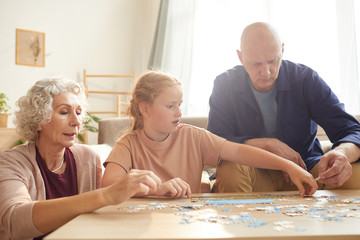 Portrait of cure red haired girl playing board games with grandparents while enjoying time together in cozy home lit by sunlight