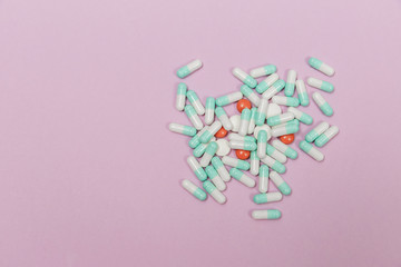 Various pills and capsules on a pink background