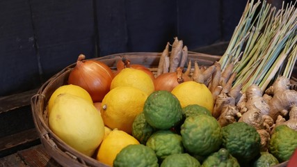 Basket with fruits and vegetables. Braided basket with various citruses and vegetables placed on floor near wooden wall