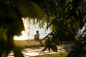 Mindfulness concept - A woman sitting by the river contemplating the sun's reflection in the water feeling relaxed