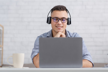 Online lessons at home during pandemic. Guy in headphones sits at table and looks in laptop