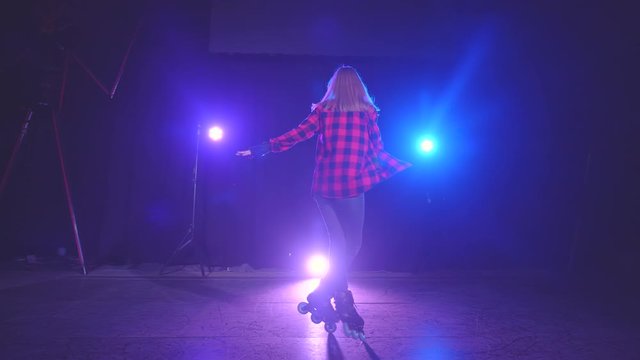 Active young attractive girl on roller skates professionally spinning on front wheels in dark scene of abandoned building under light of spotlights in close-up. Concept of sport and healthy lifestyle.