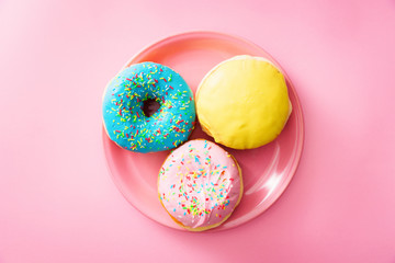 Top down view of served pink plate with colorful donuts, against pink background.