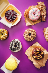 Group of various colorful chocolate donuts, on top of purple background. High angle view.