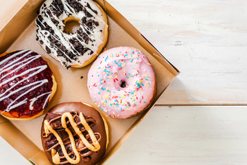 Fresh, colorful chocolate donuts, inside take away box, on top of wooden table, with negative space next to it. Top down view.