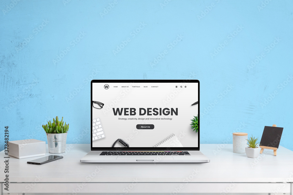 Poster Modern website of web design company presented on a laptop computer. Modern work desk with blue wall in background