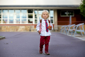 Preschool blond child, cute boy in uniform, hodling apple and book, going in preschool for the first time after summer