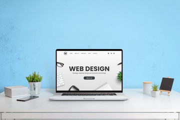Modern website of web design company presented on a laptop computer. Modern work desk with blue...