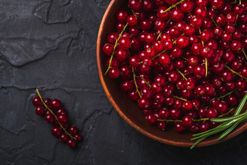 Fresh sweet red currant berries with rosemary leaves in wooden bowl, dark textured background, top view macro