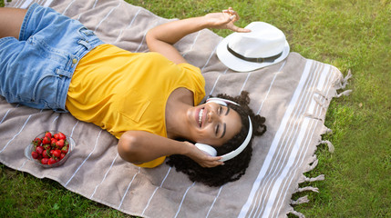 Millennial black girl listening to music in headphones during picnic at park, top view