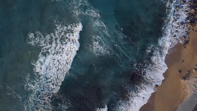 Rotating footage of waves consecutively lapping onto the shore and white bubbles remaining on the surface of beautiful blue ocean.