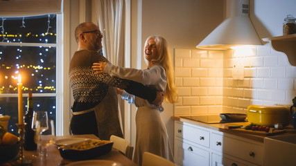 Happy Senior Couple in Love Have Romantic Evening, Dancing in the Kitchen, Celebrating Anniversary. Romantic Evening with Wine, Festive Table in Stylish Cozy Kitchen Interior