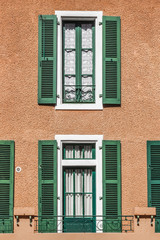 Fototapeta na wymiar Faded wooden shutters on the windows. Sun protection in hot countries and regions. Architecture in the European province. The facade of a residential building. Retro blinds. Curtains and shutters.
