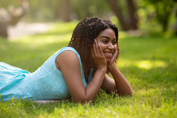 Beautiful black lady in blue dress relaxing on grass at summer park