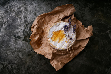 French cheese Camembert covered with honey and dried lavender stems on the paper over dark rustic background. Top view. Copy space