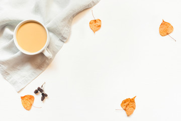 Autumn background. A cup of hot coffee or tea with milk on white wooden background with autumn leaves, napkin and cones. Copy space for text. Flat lay, top view.