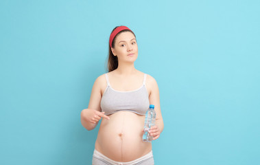 young pregnant woman with bottle of water in her hands on blue background
