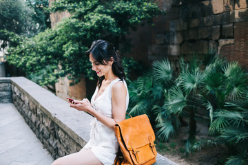 Happy lady texting on cellphone in street with garden