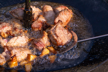 Pieces of bacon and meat are fried in a black pan
