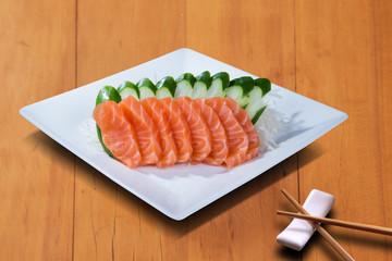 SLICES OF SALMON SASHIMI, SERVED IN A WHITE PLATE, ON THE WOODEN BACKGROUND