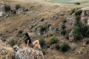 Young woman with a backpack, sitting on the top of a mountain, relaxing. Travel concept.