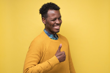 Handsome black man wiking shoing thumb up. Studio shot on yellow wall.