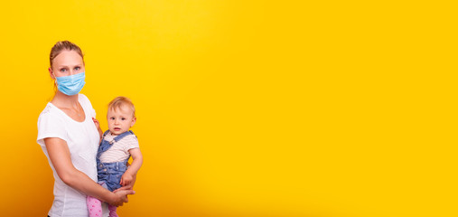Mutter mit Mundschutz hält ihre Tochter vor gelben Hintergrund auf dem Arm