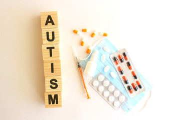 The words AUTISM is made of wooden cubes on a white background with medical drugs and medical mask. Medical concept.