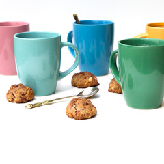 Many multi-colored mugs of lemon tea and homemade cookies on a white table.