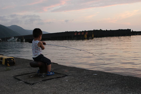夕暮れの港で堤防釣りをする男の子（幼児）