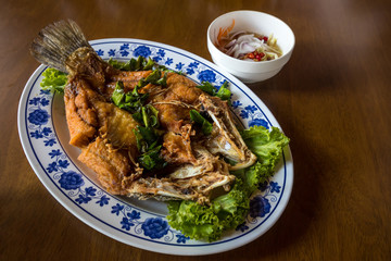 Fried sea bass fish in white plate with spicy and sweet sauce in Thai style .  crispy Thai style deep fried whole sea bass fish served with spicy mango sauce. crispy deep fried sea bass 