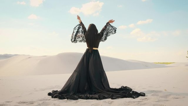  Beauty a woman, rear view. Queen in black clothes dancing in desert. Girl fashion model. long silk arab dress. Back of luxury elegant goddess. backdrop a white sand, blue sky. Mysterious silhouette