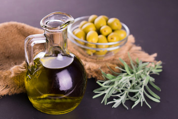 Olive oil in a bottle and fresh rosemary on a dark background.