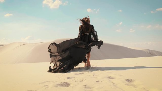 Silhouette of a happy woman running in the desert. Long black silk dress and hair flying fluttering in the wind in slow motion. A tourist is enjoying a vacation in the Dubai desert. Video footage 4K