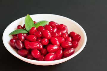 Red dogwood berries in a plate on a black background.
Close-up.