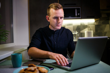 Fototapeta na wymiar A freelancer works from home in the kitchen and using a laptop. Successful man working with a laptop and reading good news. Handsome successful entrepreneur sits and works in his modern home.
